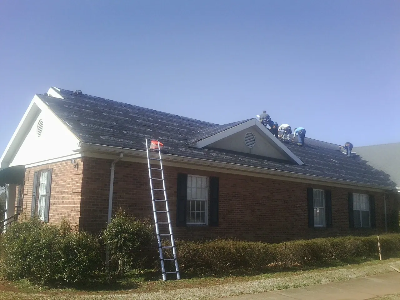 Crew tearing shingles off a brick ranch roof with a ladder set — Emergency Roof Repair work by our crew in Forestville