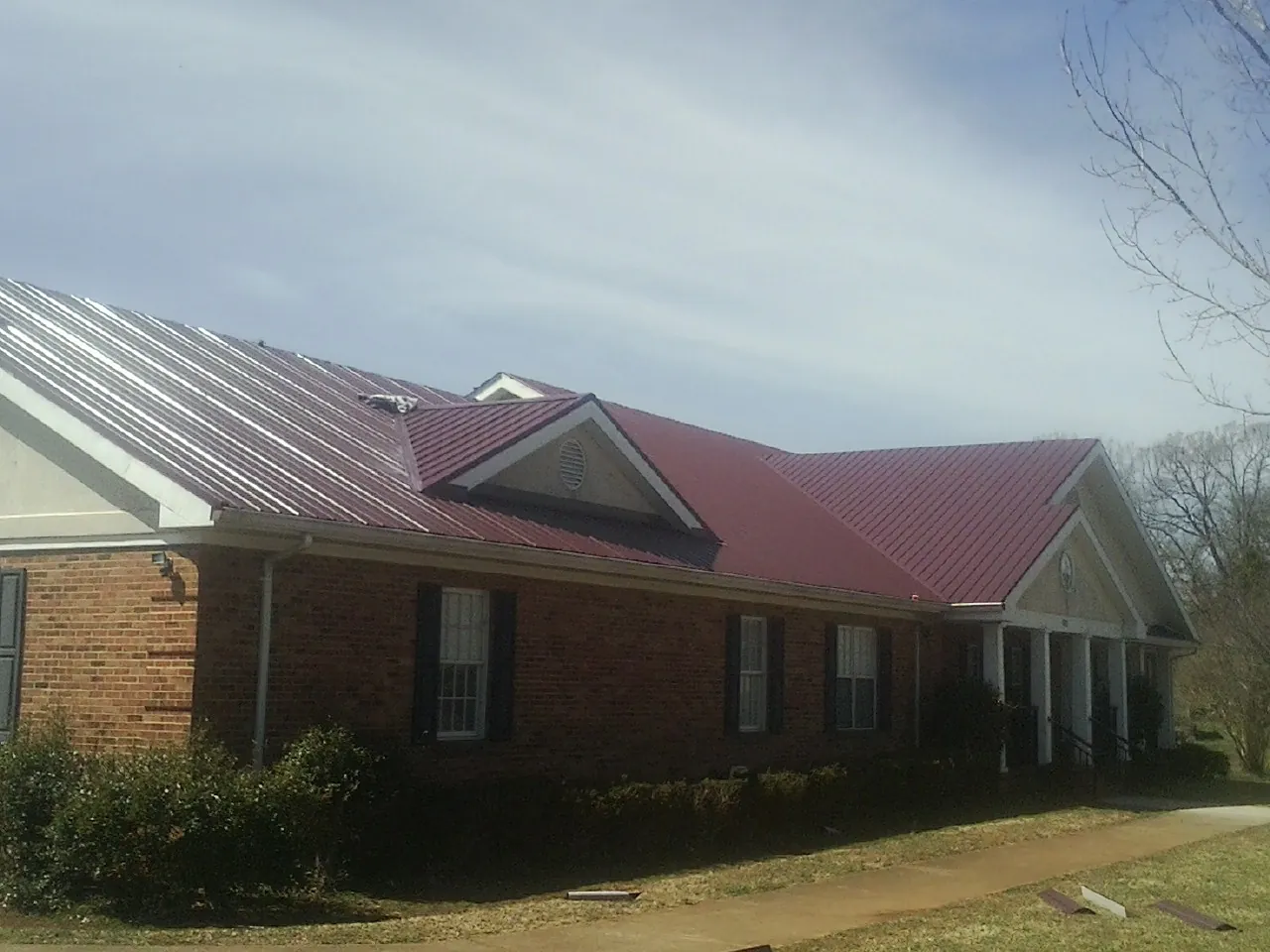 Red metal roof with gabled entries on a long brick building, from a Hail Damage Roof Repair job in Forestville