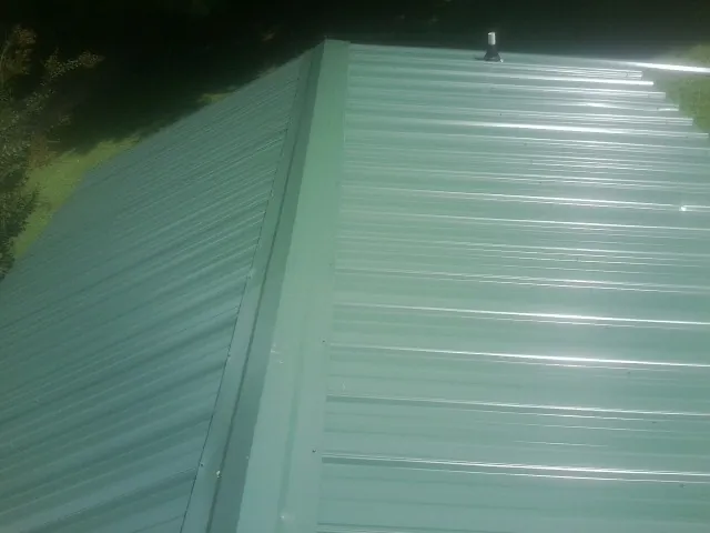 New green metal panels meeting at the ridge of a roof — Flat Roof Repair work by our crew in Forestville