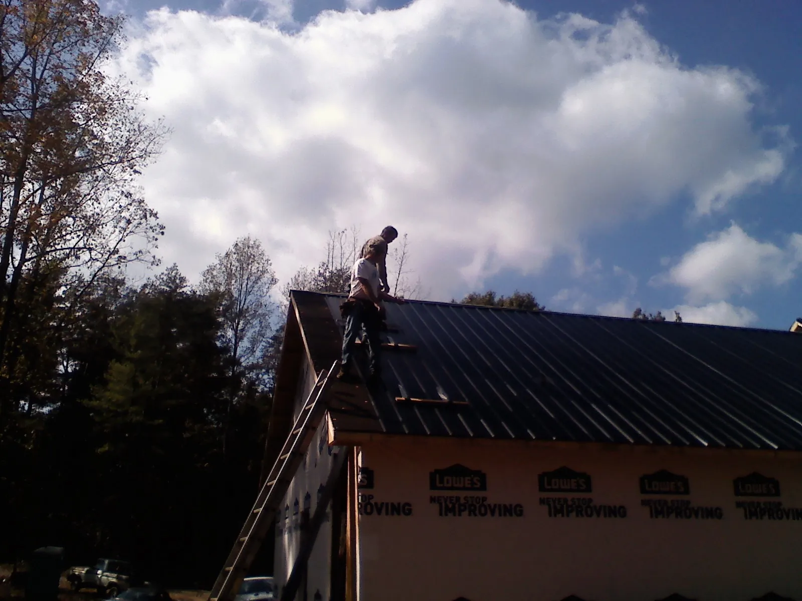 Roofer fastening dark metal panels high against a cloudy sky, from a Roof Inspection job in Forestville
