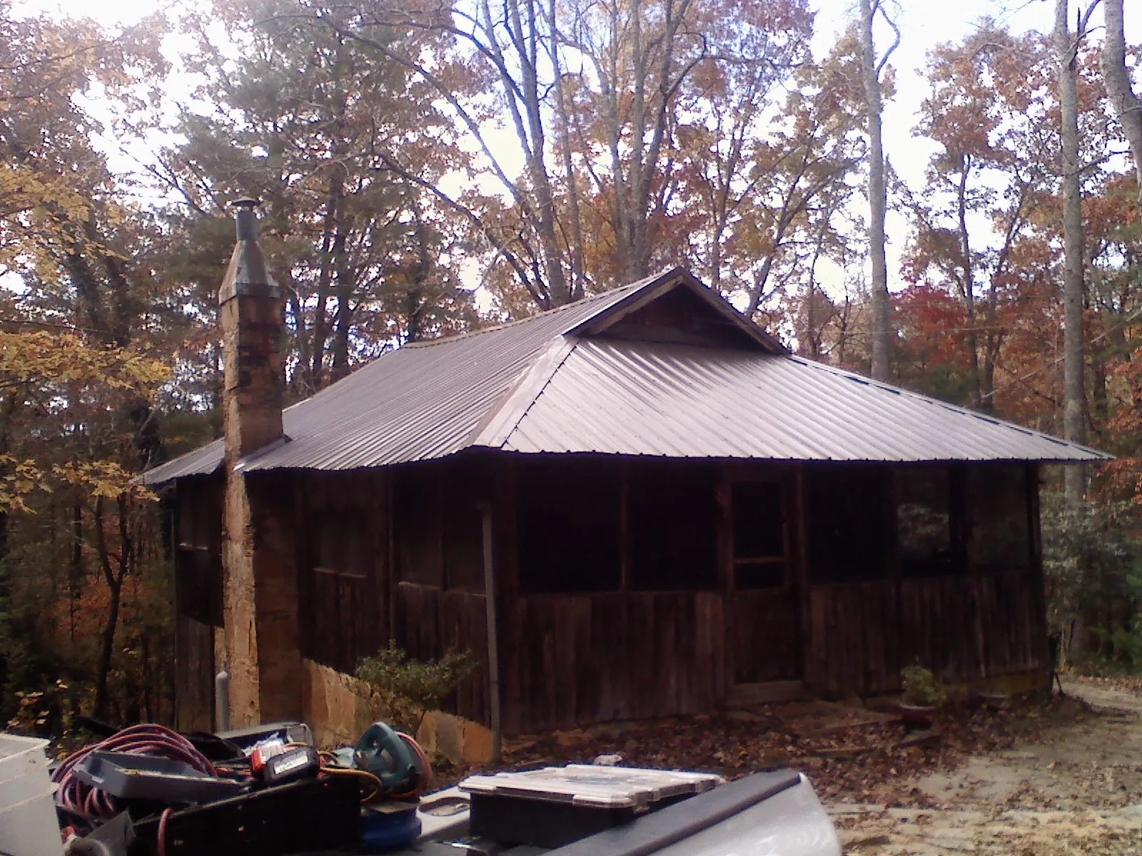 Brown metal hip roof on an old cabin with a stone chimney in Forestville